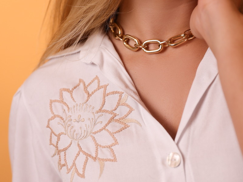 Detalhe do bordado de flor de cacto no ombro de uma camisa branca da coleção