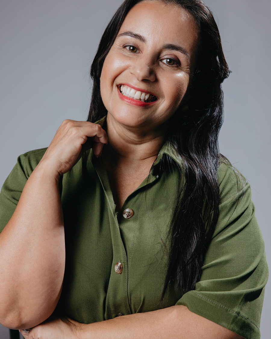 Retrato de Karla Duarte sorrindo, em camisa verde, no estúdio